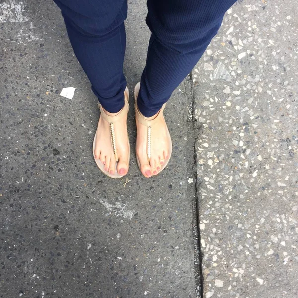 Закрыть ноги с коричневым ногтем в золотых сандалиях и синих штанах на женских ногах на заднем плане — стоковое фото