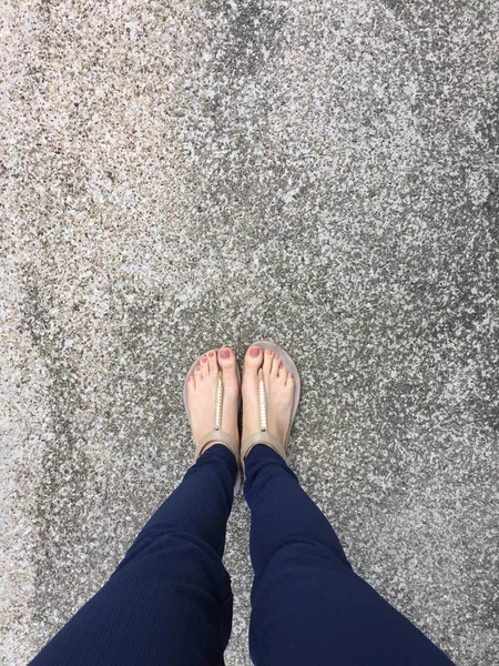 Feche o pé com prego marrom em sandálias de ouro e calça azul nos pés femininos no fundo do terreno — Fotografia de Stock