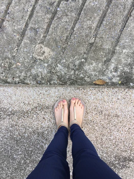 Close-up van de voeten met bruin nagel in gouden sandalen en blauwe broek op vrouwelijke voeten op de grond achtergrond — Stockfoto