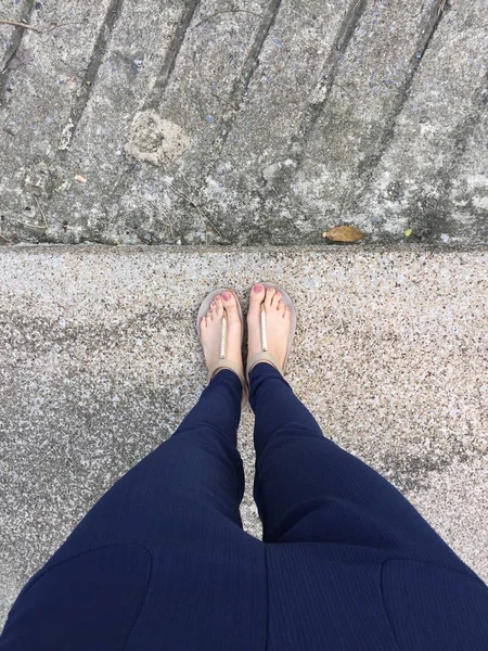 Nahaufnahme Füße mit braunem Nagel in goldenen Sandalen und blauer Hose an weiblichen Füßen auf dem Boden Hintergrund — Stockfoto