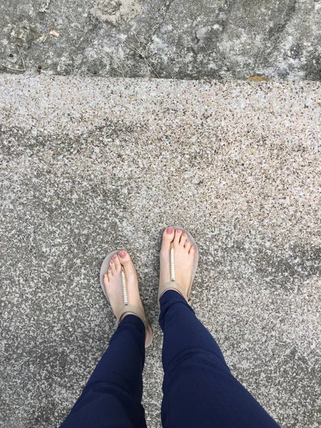 Stäng upp fötterna med brun spik i guld sandaler och blå byxor på kvinnliga fötter på marken bakgrund — Stockfoto