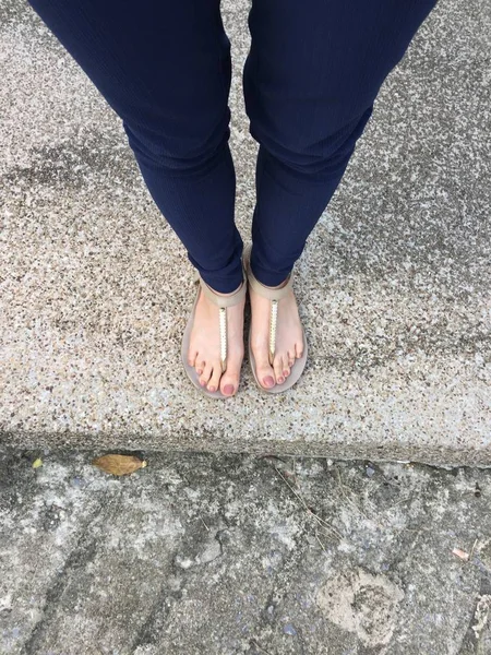Detailní záběr nohou s hnědý hřebík v zlaté sandály a modré kalhoty na ženské nohy na zem pozadí — Stock fotografie