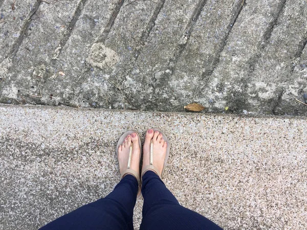 Fermer Pieds avec Clou Marron en Sandales Or et Pantalon Bleu sur Pieds Féminins sur fond de Terre — Photo