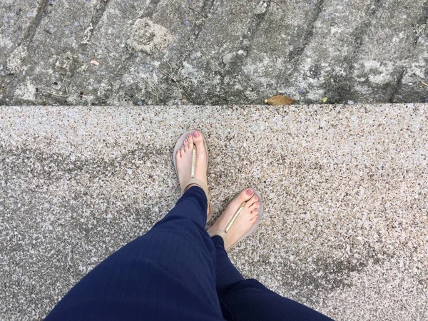 Stäng upp fötterna med brun spik i guld sandaler och blå byxor på kvinnliga fötter på marken bakgrund — Stockfoto