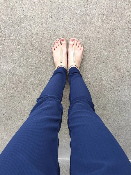 골드 샌들과 지상 배경에 여성 발에 파란 바지에 갈색 손톱으로 피트를 닫습니다 — 스톡 사진