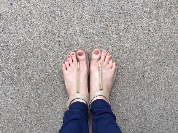 Pies de cerca con clavo marrón en sandalias de oro y pantalones azules en los pies femeninos en el fondo del suelo — Foto de Stock