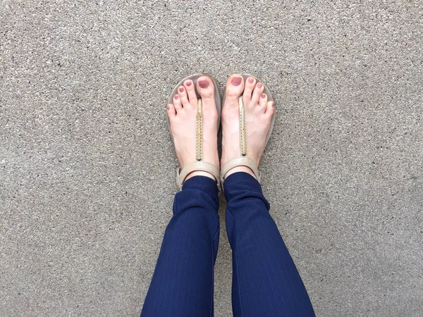 特写脚与棕色钉子在黄金凉鞋和蓝色裤子在女性脚在地面背景 — 图库照片
