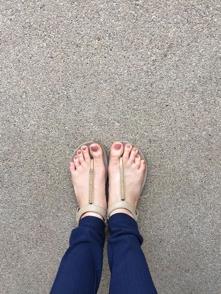 Feche o pé com prego marrom em sandálias de ouro e calça azul nos pés femininos no fundo do terreno — Fotografia de Stock