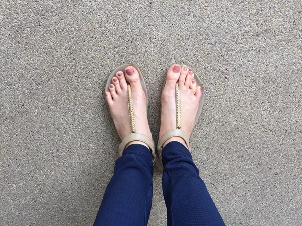 特写脚与棕色钉子在黄金凉鞋和蓝色裤子在女性脚在地面背景 — 图库照片
