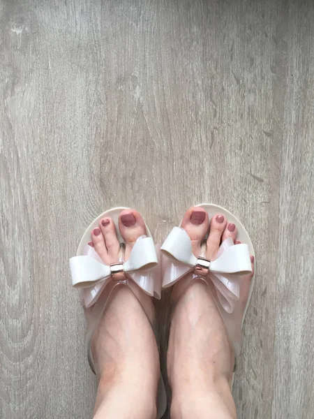 Жіночі ноги і ноги з педикюр в рожеві тапочки на дерев'яну підлогу — стокове фото