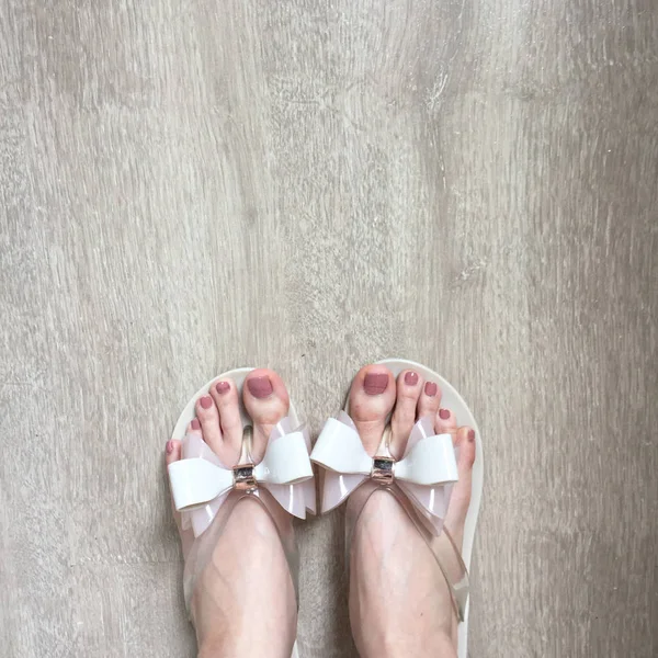 Ženské nohy a nohy s pedikúru v růžové pantofle na dřevěnou podlahu — Stock fotografie