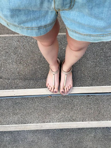 Jong meisje voeten met bruine nagels in gouden sandalen op trap achtergrond — Stockfoto