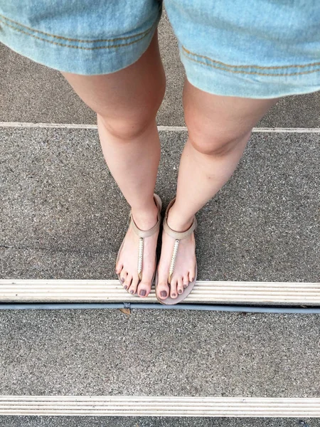 Jong meisje voeten met bruine nagels in gouden sandalen op trap achtergrond — Stockfoto