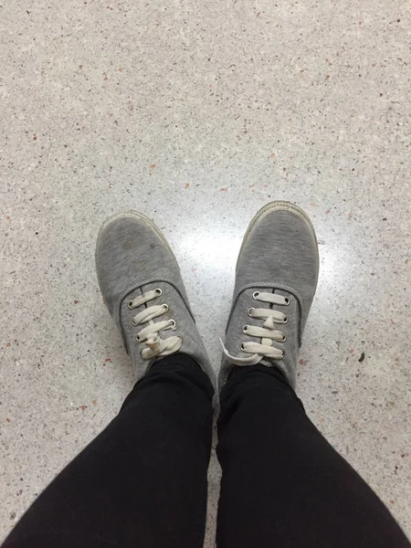 Piernas de mujer de moda joven en pantalones vaqueros negros y zapatillas grises en el piso — Foto de Stock