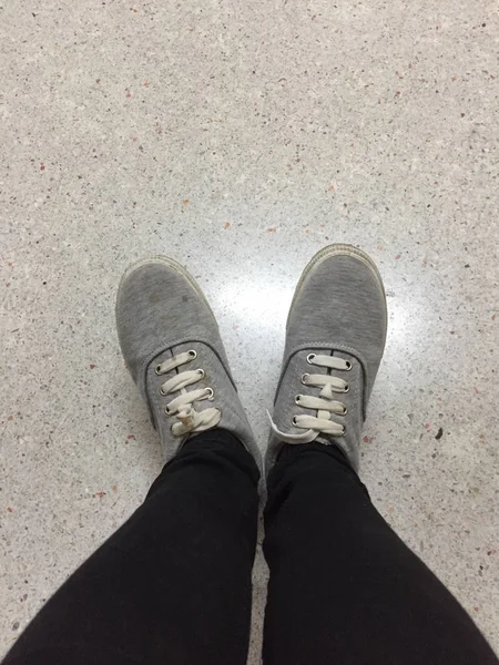 Piernas de mujer de moda joven en pantalones vaqueros negros y zapatillas grises en el piso —  Fotos de Stock