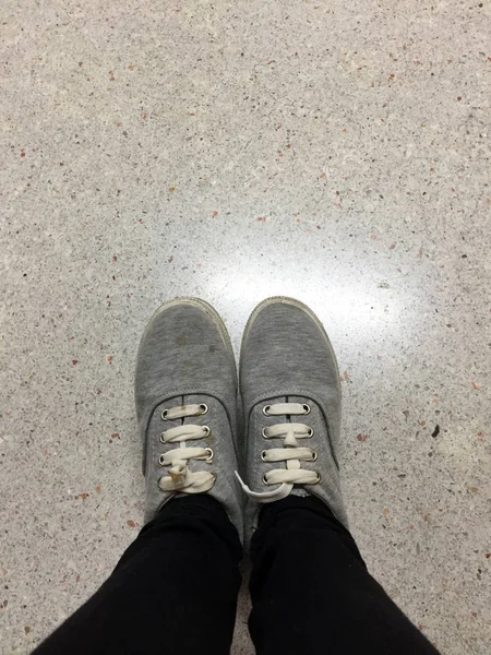 Ungt mode kvinnans ben i svarta Jeans och grå Sneakers på golvet — Stockfoto