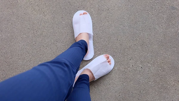Genç kadın bacaklar ve ayaklar yere, kapalı arka plan beyaz terlik ve Mavi pantolon giyiyor