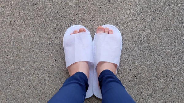 Genç kadın bacaklar ve ayaklar yere, kapalı arka plan beyaz terlik ve Mavi pantolon giyiyor