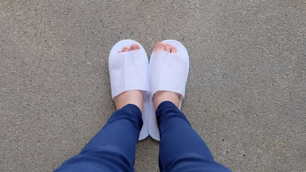 Genç kadın bacaklar ve ayaklar yere, kapalı arka plan beyaz terlik ve Mavi pantolon giyiyor