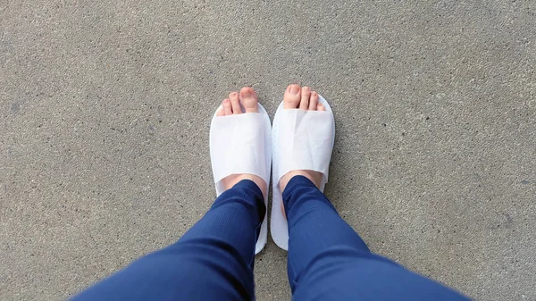 Genç kadın bacaklar ve ayaklar yere, kapalı arka plan beyaz terlik ve Mavi pantolon giyiyor