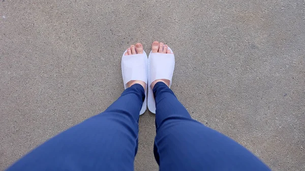 Genç kadın bacaklar ve ayaklar yere, kapalı arka plan beyaz terlik ve Mavi pantolon giyiyor