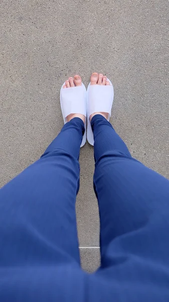 Jeunes femmes Jambes et pieds portant des pantoufles blanches et des pantalons bleus au sol, Fond intérieur — Photo