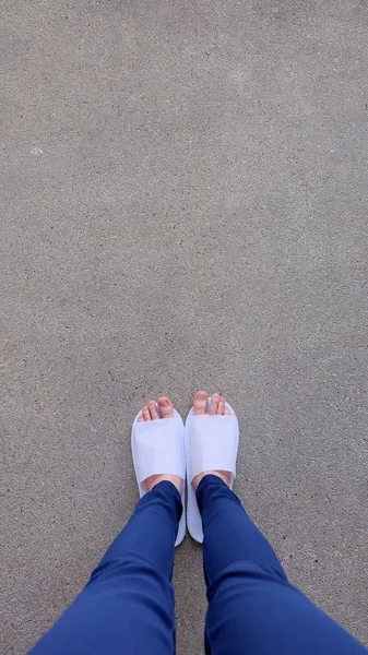 Young Females Legs and Feet Wearing White Slippers and Blue Pants on Ground, Indoor Background — Stock Photo, Image