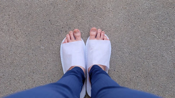 Mladé samice nohy a chodidla, na sobě bílé pantofle a modré kalhoty na zem, krytý pozadí — Stock fotografie