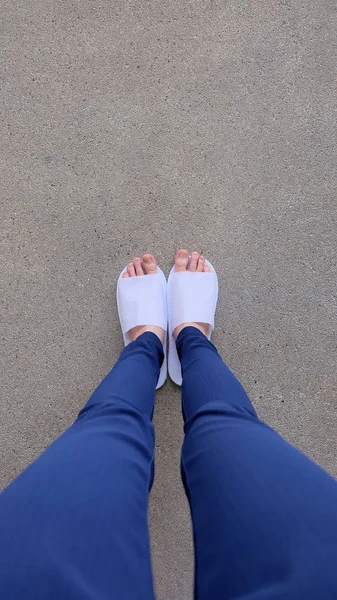 Jeunes femmes Jambes et pieds portant des pantoufles blanches et des pantalons bleus au sol, Fond intérieur — Photo