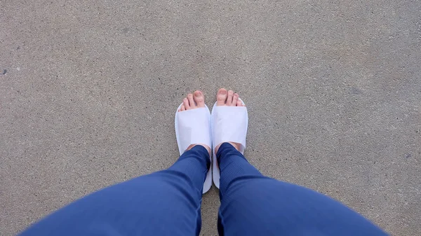 Unga kvinnor ben och fötter som bär vita tofflor och blå byxor på marken, inomhus bakgrund — Stockfoto