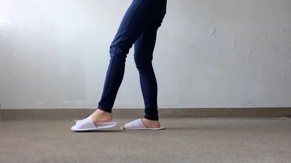 Jonge vrouwen benen en voeten dragen witte Slippers en blauwe broek op grond, overdekt achtergrond — Stockfoto