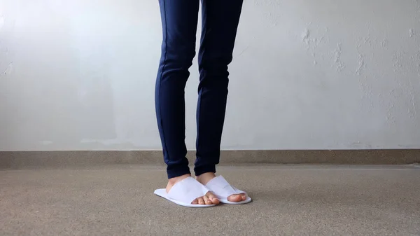 Νεαρά θηλυκά πόδια και τα πόδια, φορώντας παντόφλες λευκό και μπλε παντελόνι στο έδαφος, εσωτερική φόντο — Φωτογραφία Αρχείου