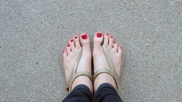 Närbild på flickans fötter bär gyllene sandaler på marken bakgrund — Stockfoto
