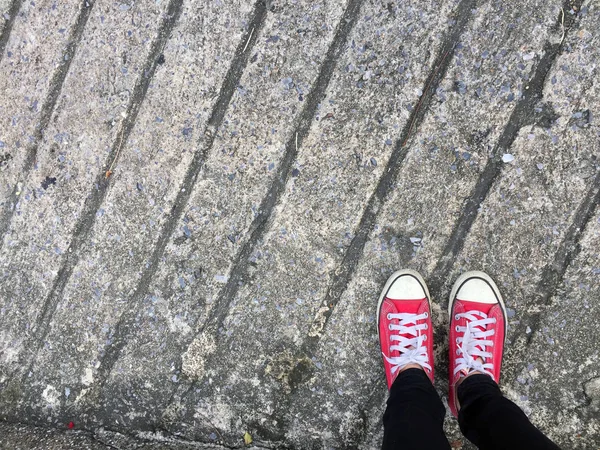 Foto di primo piano della donna che indossa scarpe da ginnastica rosse sullo sfondo del pavimento in cemento — Foto Stock