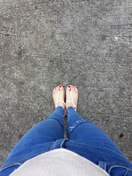 Close up of Bare Feet with Red Nail in Sandals and Blue Jeans Woman on the Concrete Floor Background — стоковое фото