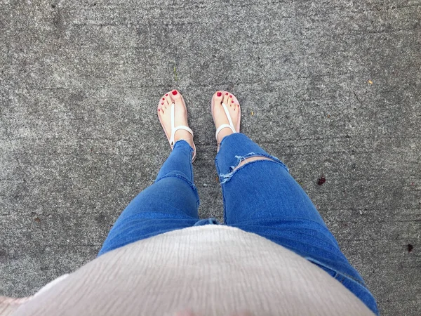 Nahaufnahme von nackten Füßen mit rotem Nagel in Sandalen und Blue Jeans Frau auf dem Betonboden Hintergrund — Stockfoto