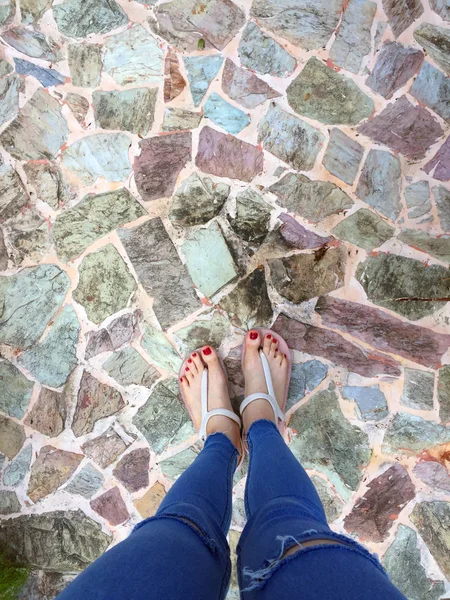 Kırmızı tırnak sandalet ve Mavi Jeans kadın üzerinde döşeme arka planı çıplak ayakla, yakın çekim