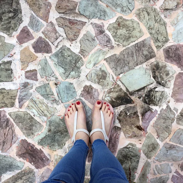 Gros plan de pieds nus avec ongle rouge dans des sandales et jeans bleu femme sur le fond carrelage — Photo