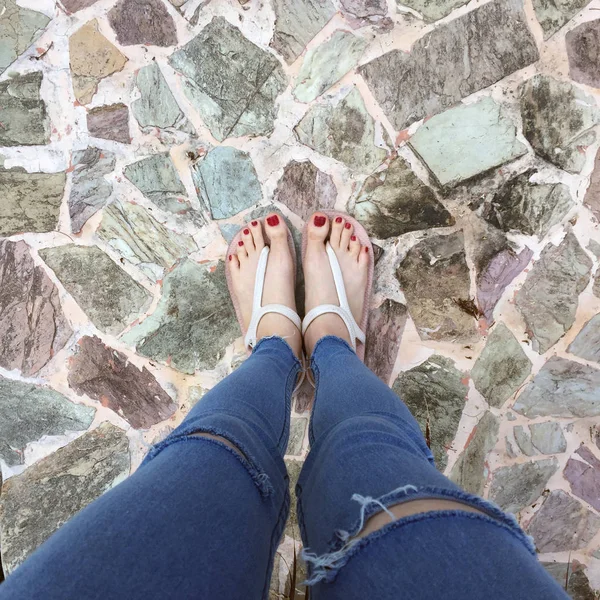 Primo piano di piedi nudi con chiodo rosso in sandali e Blue Jeans donna sullo sfondo piastrelle — Foto Stock