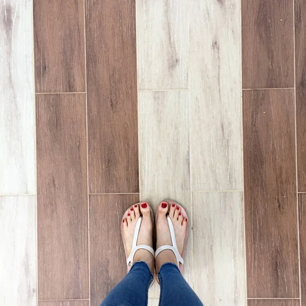 Gros plan de pieds nus avec ongle rouge dans des sandales et jeans bleu femme sur le fond carrelage — Photo