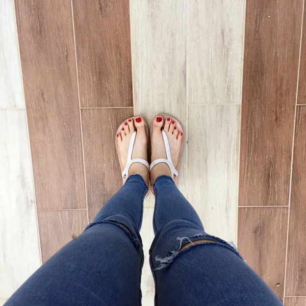 Gros plan de pieds nus avec ongle rouge dans des sandales et jeans bleu femme sur le fond carrelage — Photo