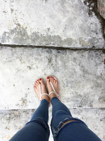 Close up van blote voeten met rode nagel in sandalen en spijkerbroek vrouw op de betonnen vloer achtergrond — Stockfoto