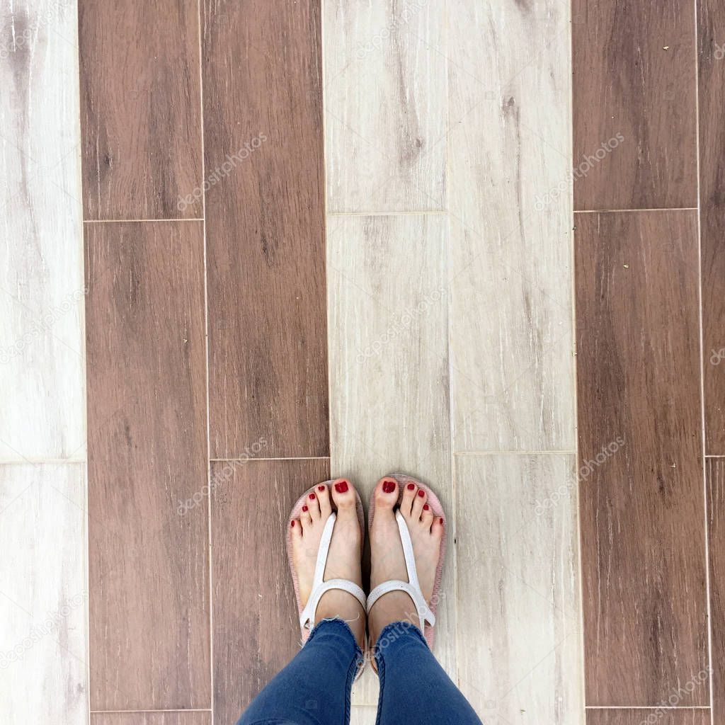 Close up of Bare Feet with Red Nail in Sandals and Blue Jeans Woman On The Tile Background
