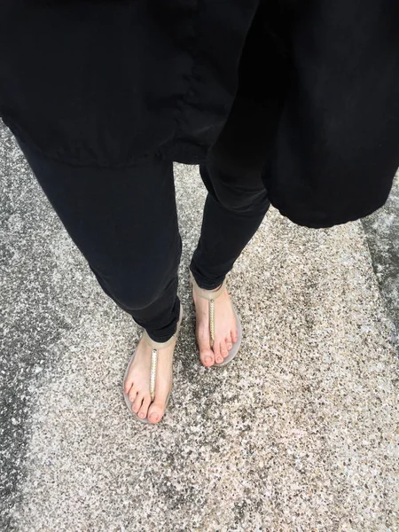 Close Up on Girl 's Feet Wearing Golden Sandals and Black Jeans On The Concrete Background — стоковое фото