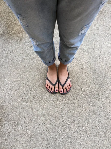 Närbild på flickans fötter bär svarta sandaler och blå Jeans på gatan — Stockfoto