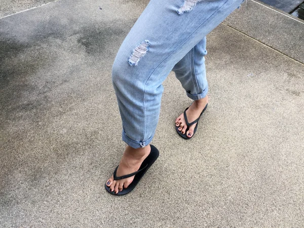 Närbild på flickans fötter bär svarta sandaler och blå Jeans på gatan — Stockfoto