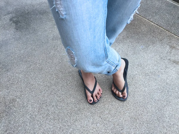 De cerca en los pies de la muchacha con sandalias negras y pantalones vaqueros azules en la calle — Foto de Stock