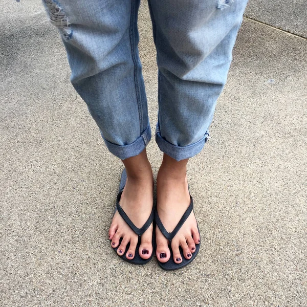 De cerca en los pies de la muchacha con sandalias negras y pantalones vaqueros azules en la calle —  Fotos de Stock