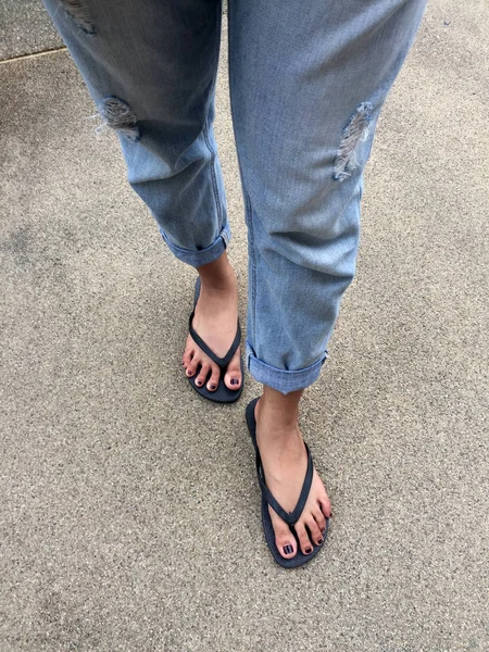 De cerca en los pies de la muchacha con sandalias negras y pantalones vaqueros azules en la calle —  Fotos de Stock