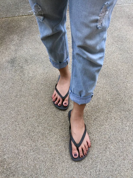 Nahaufnahme an Mädchenfüßen in schwarzen Sandalen und blauen Jeans auf der Straße — Stockfoto
